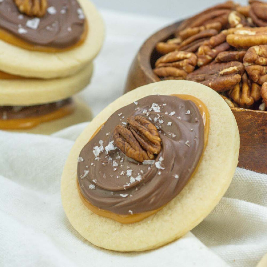 pecan turtle cookie leaning against a container of pecans