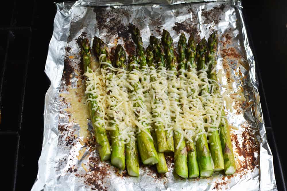 Grilled asparagus on grill covered in melted cheese