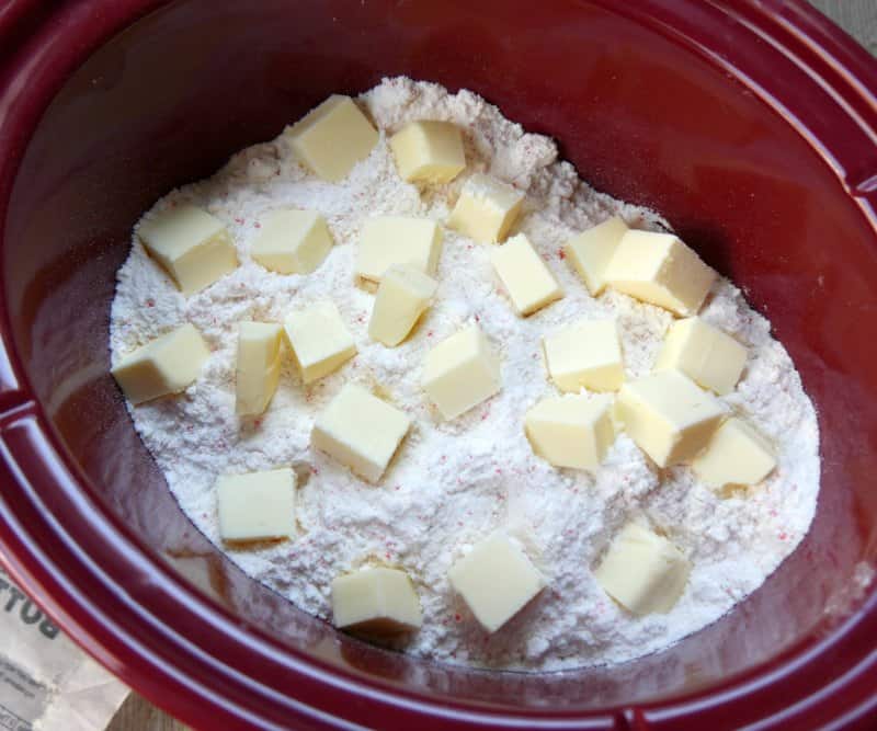 Cubed butter on top of cake mix in a red oval slow cooker