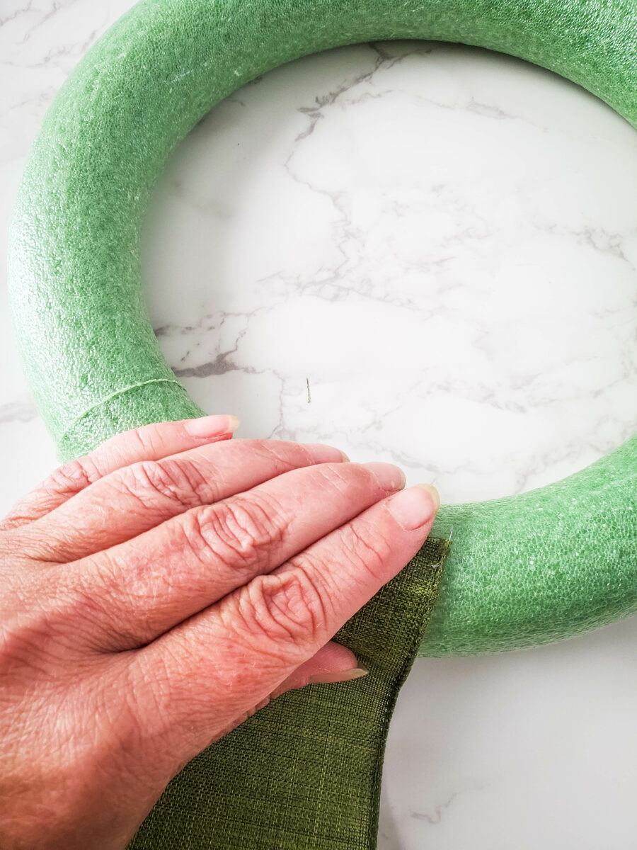 A hand holding one end of ribbon to the gnome wreath form