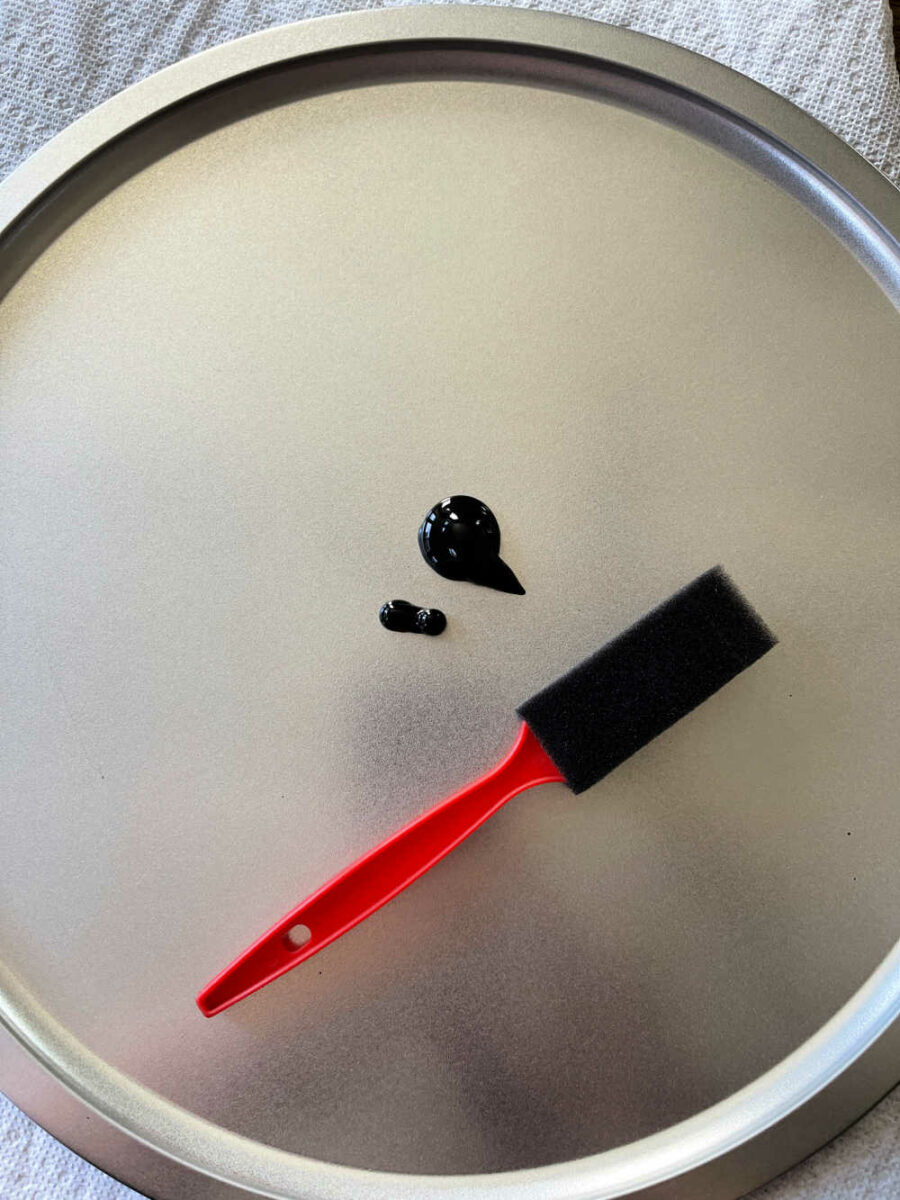 Pizza pan with black paint and a paint brush on it.