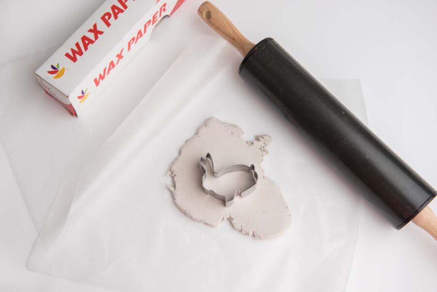 Bunny cookie cutter white clay on top of wax paper with rolling pin 