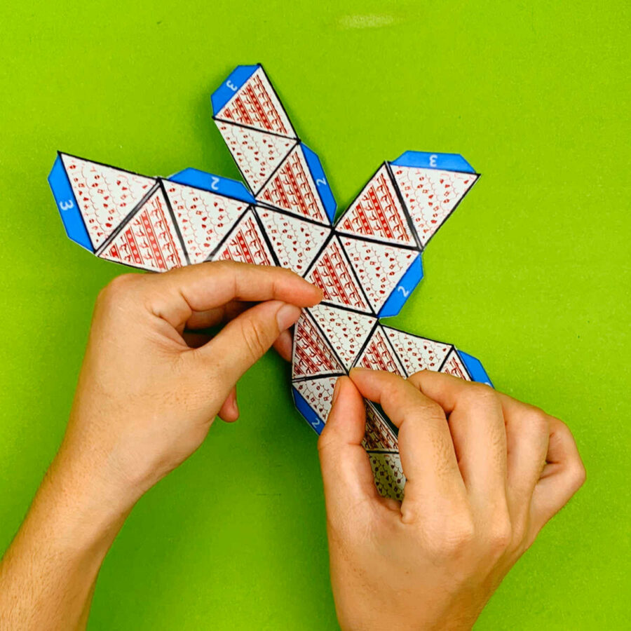 A person folding a print and fold paper Christmas tree ornament craft