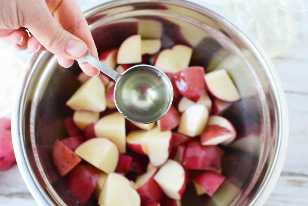 Tabelspoon of oil over a bowl of red potatoes