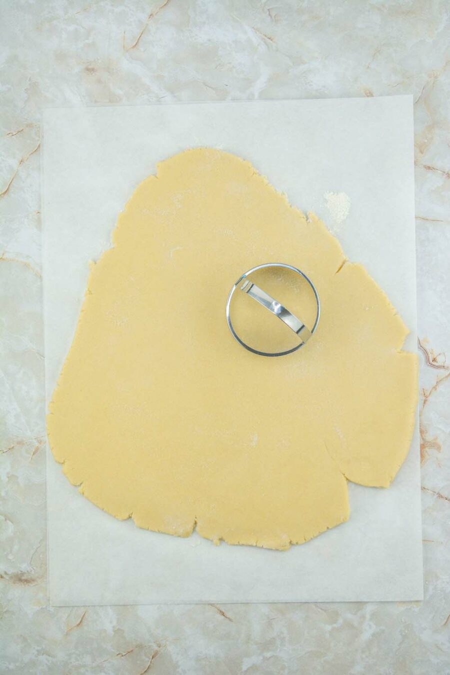 Cookie dough rolled out on parchment paper with a cookie cutter on top