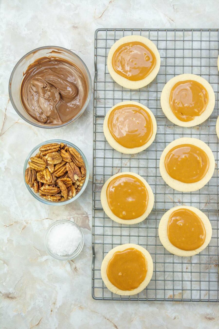 Baked cookies with caramel sauce on top with bowls of melted chocolate and pecans on the side
