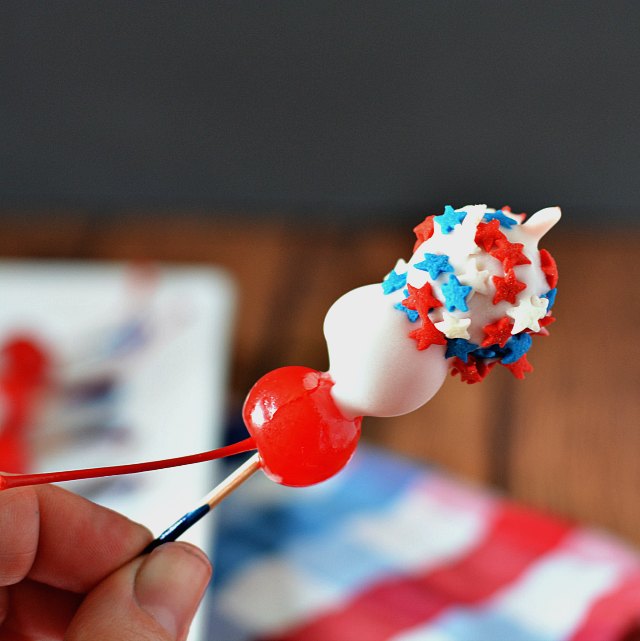 3 maraschino cherries on a toothpick, partly dipped in white chocolate with red white and blue star sprinkles on one cherry