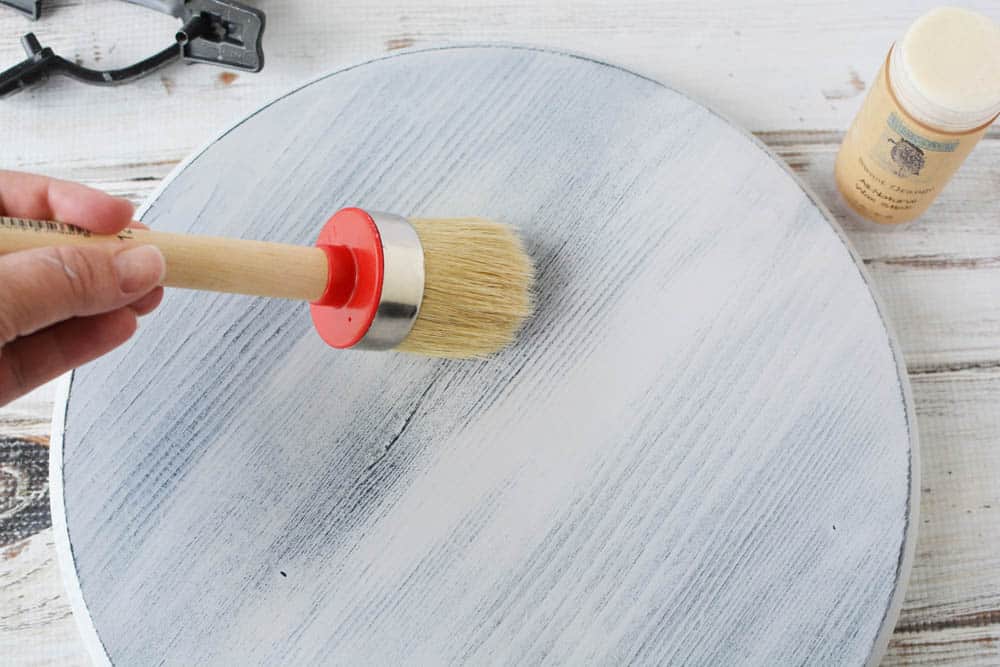 chalk paint wax being put on a painted and distressed wood circle