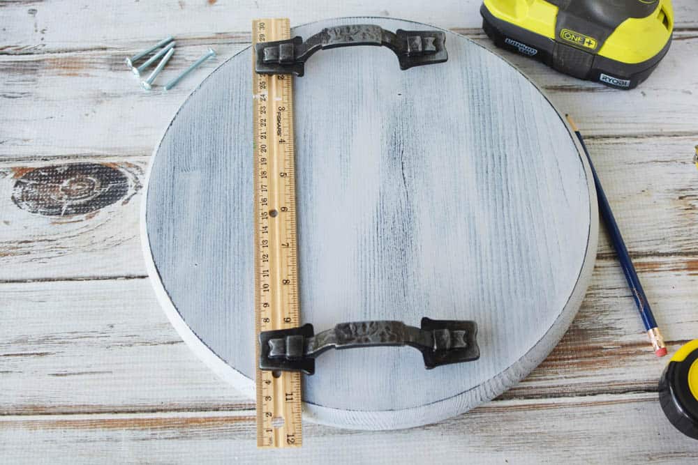 a wood circle with 2 drawer handles and a ruler showing where to put the handles