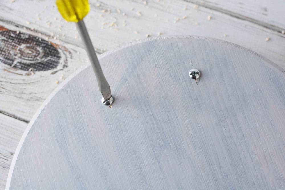 a screwdriver screwing in screws to a wood circle tray