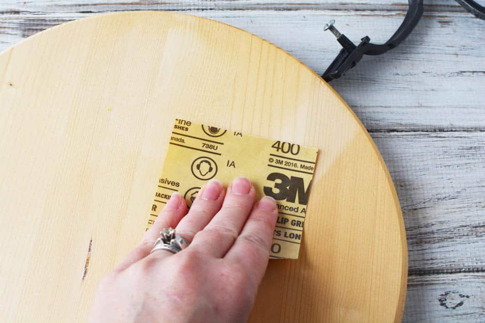 a hand sanding a wood circle with sand paper