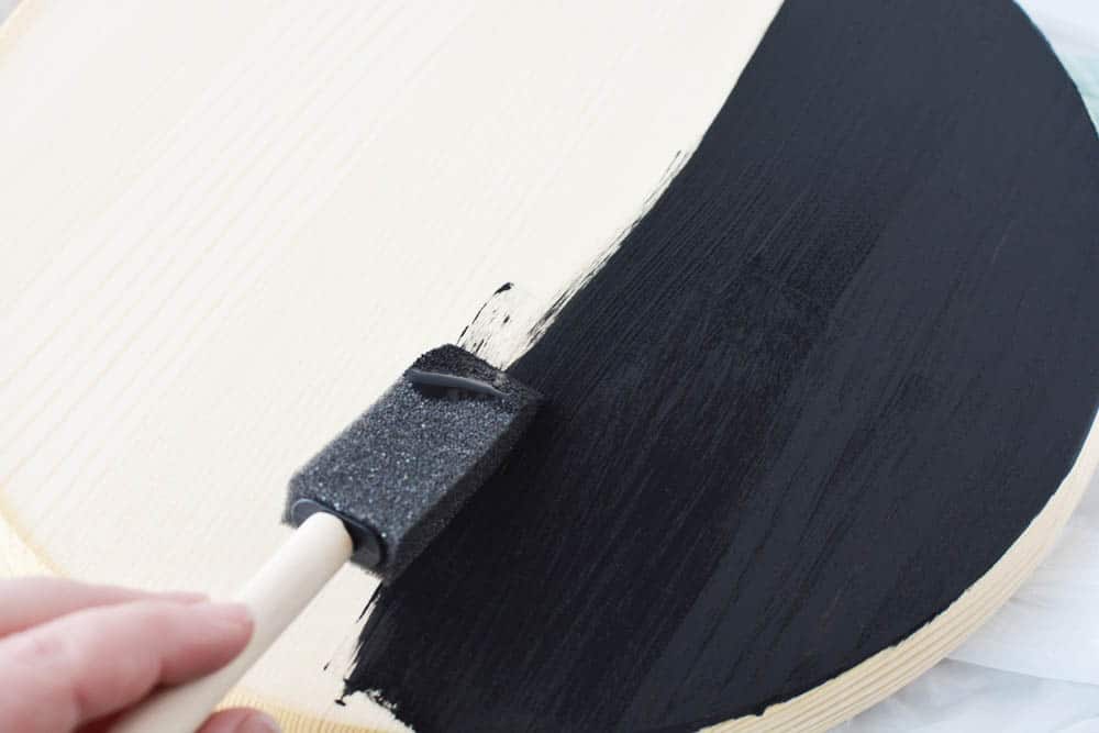 someone painting a wood circle black with a sponge brush