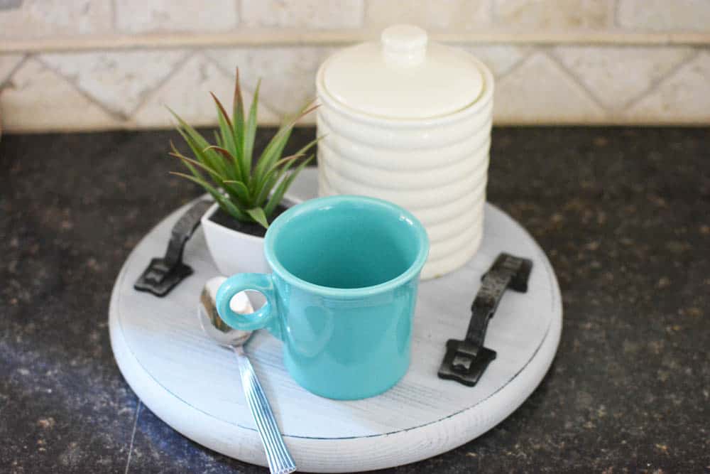 turquoise cup sitting on top of a wood tray along with a small plant and a whit cansiter