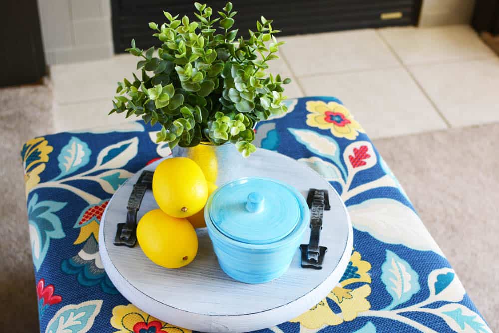 wood tray on a floral ottoman with lemons, plant and turquoise canister on it